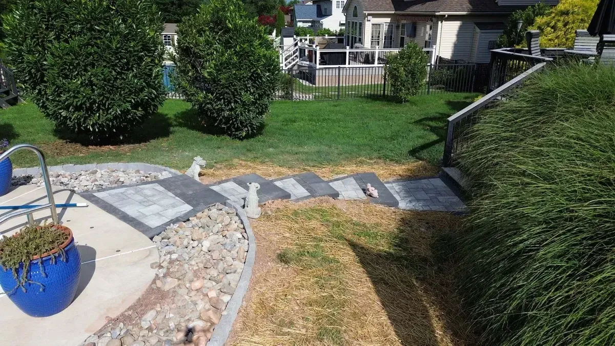Paver walkway connecting pool deck to backyard with river rock edging in Chester County PA