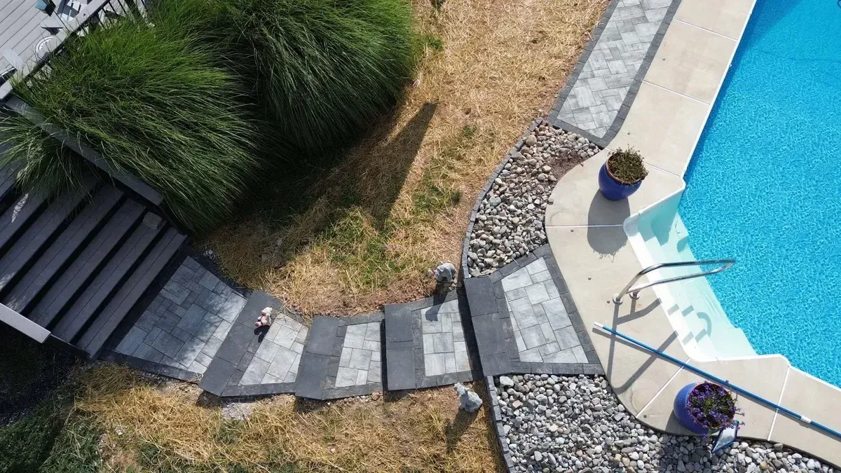 Aerial view of paver steps leading to pool deck with river rock border in Chester County PA